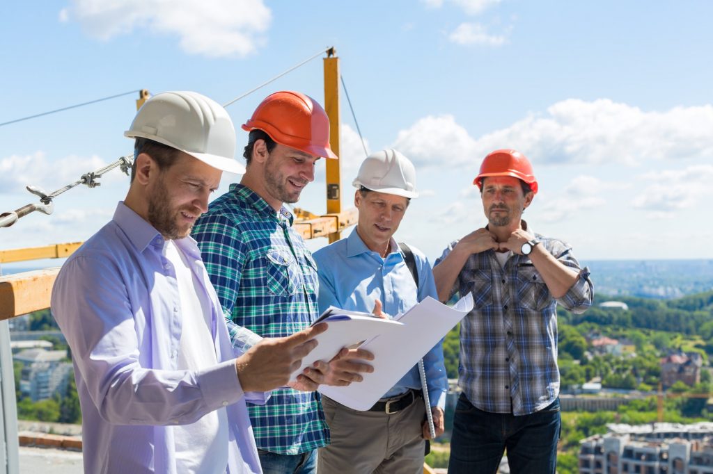 Group Of Builders In Hardhats Meeting On Construction Site Building Team Working With Plan Engineer